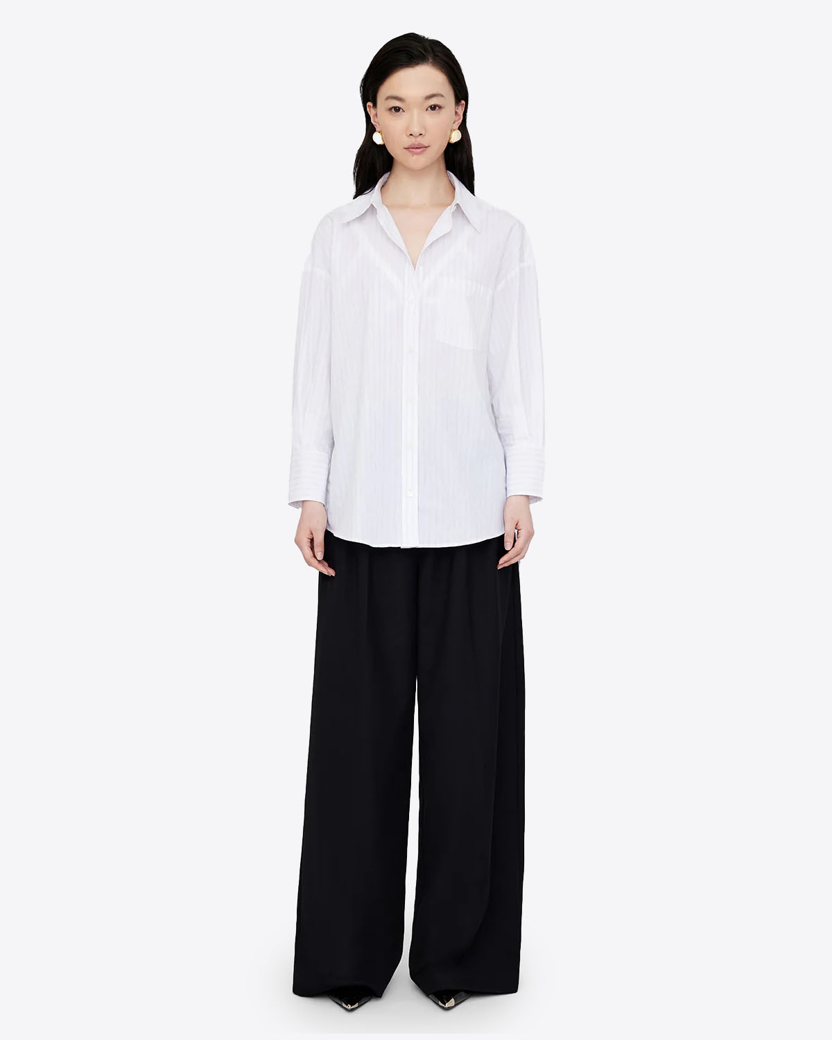 Chemise blanche manches longues Mika Anine Bing à rayures noires. Vue face. Portée avec un pantalon noir. 