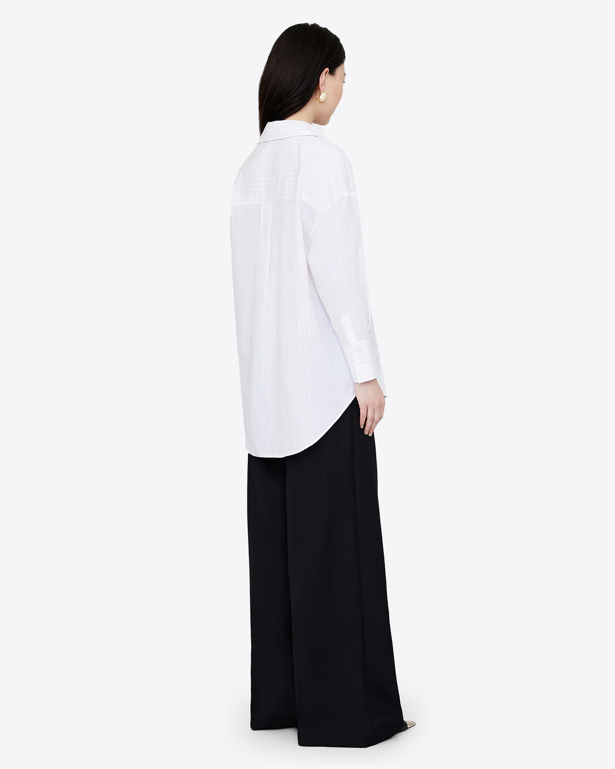 Chemise blanche manches longues Mika Anine Bing à rayures noires. Vue trois quart dos. Portée avec un pantalon noir. 