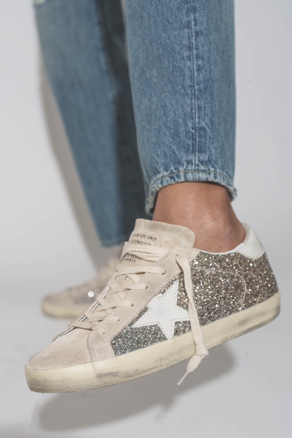 Sneakers Superstar à paillettes argent et or étoile en cuir blanc 55636 Golden Goose Femme. Porté avec un jean bleu.