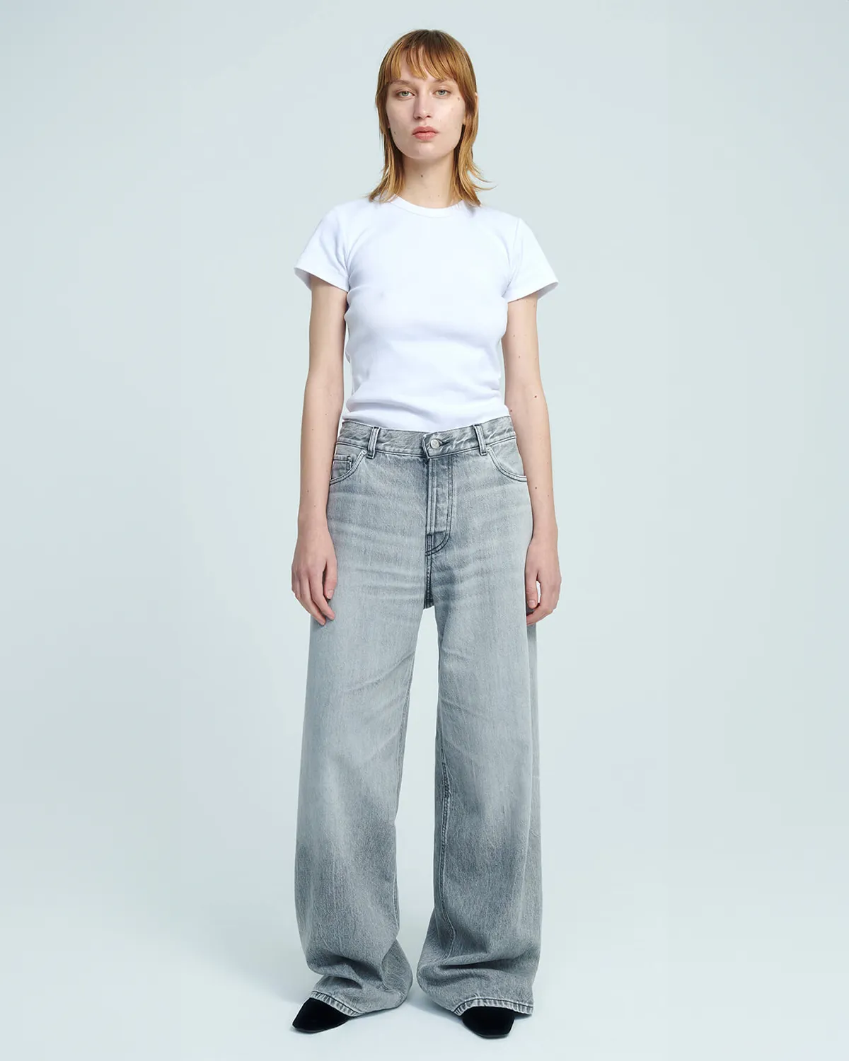 Jean large taille basse délavage gris clair Bethany Haikure. Porté avec un tee-shirt blanc.