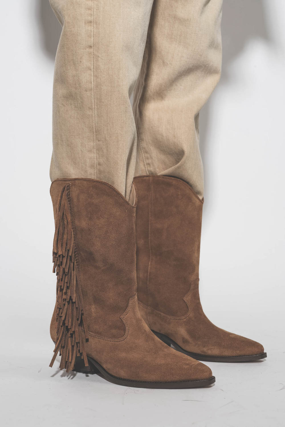 Bottes en cuir suédé marron forme santiag avec des franges sur les côtés Duerto Isabel Marant. Porté avec un jean Crossover beige. Détail des franges. 