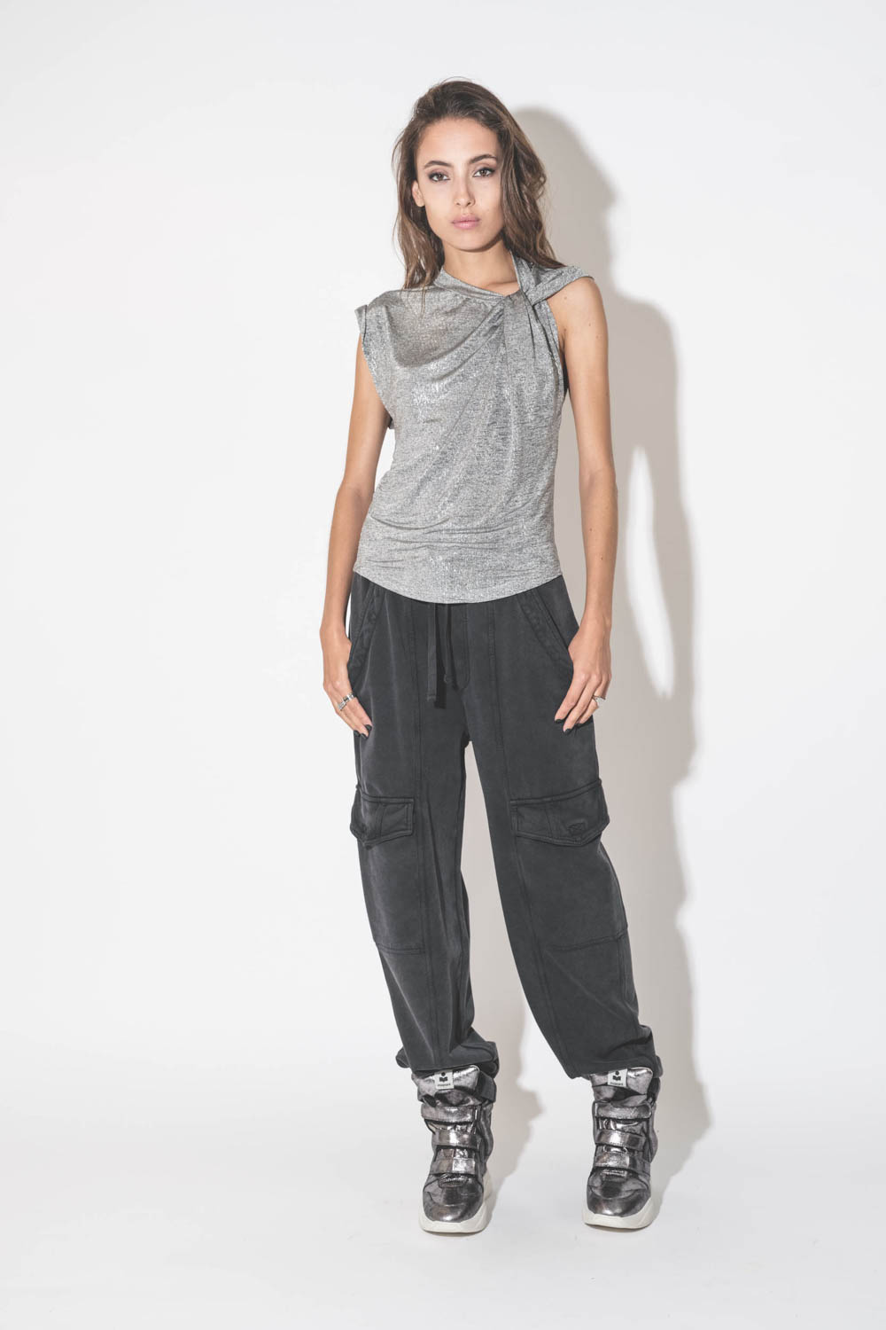 Top drapé sans manches asymétrique en jersey lamé argent Naylor Isabel Marant Etoile. Porté avec un bas de jogging noir. 