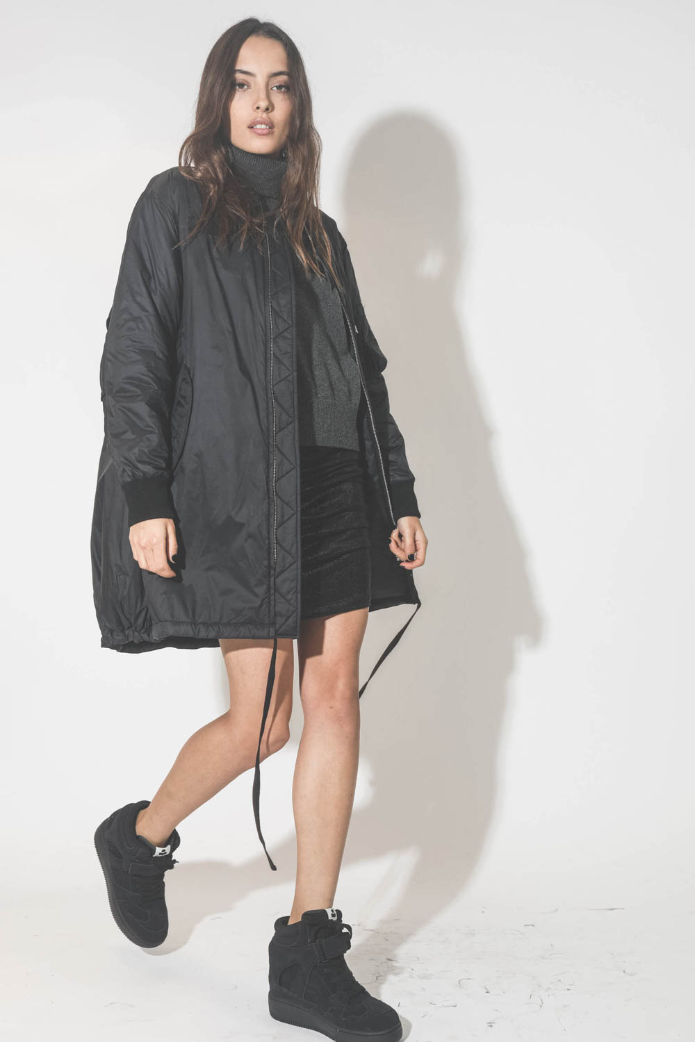 Manteau Bomber long noir Vis à Vis. Porté avec des sneakers compensées.